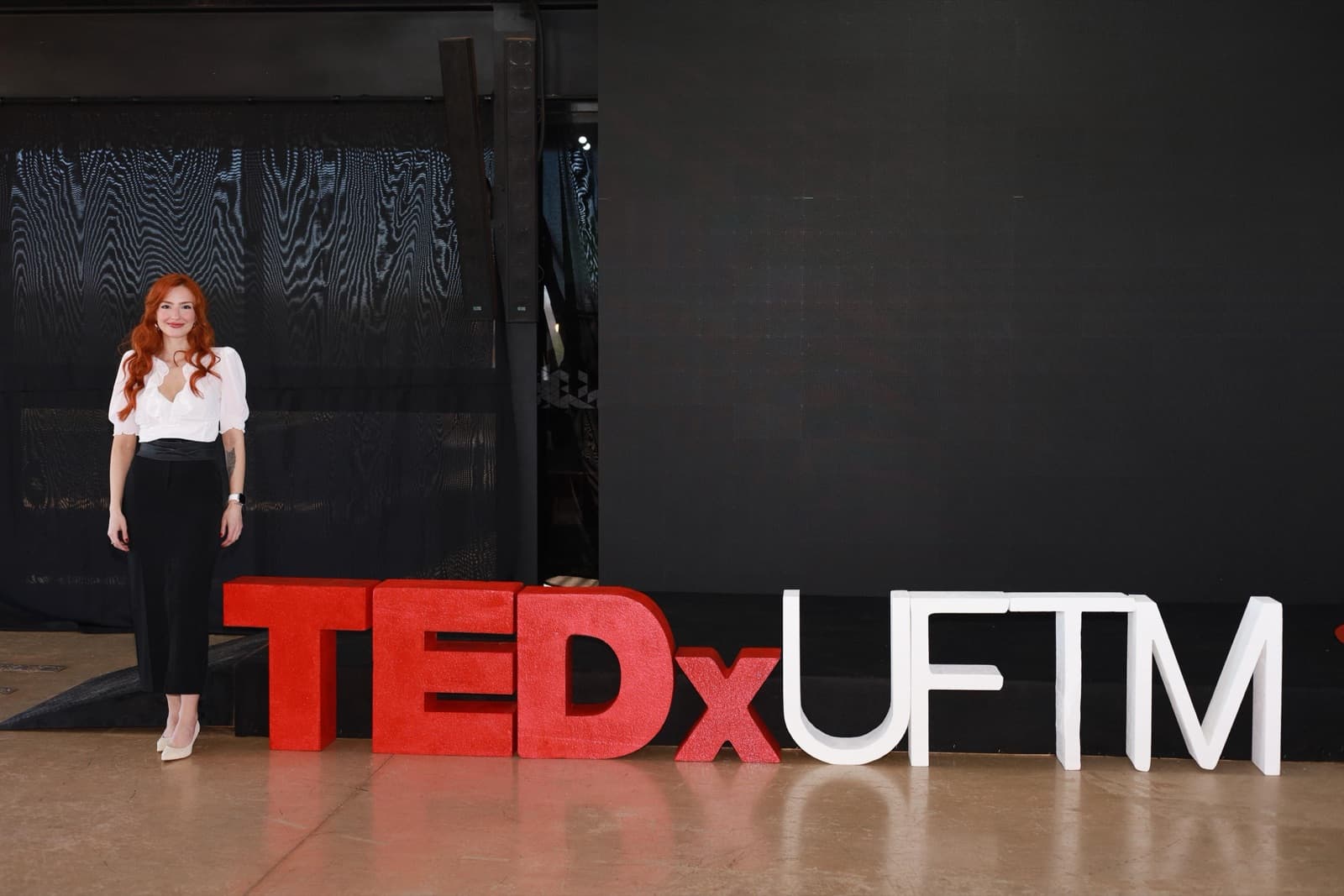 Eu em pé ao lado das letras gigantes TEDxUFTM, no palco vazio.