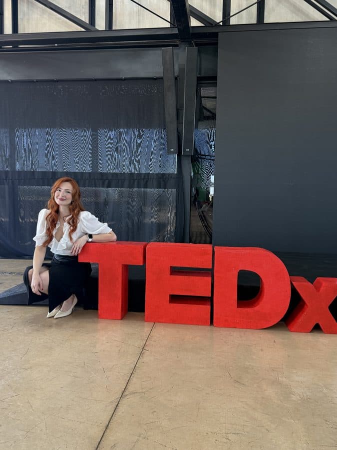 Eu sentada ao lado das letras gigantes do TEDx, nos bastidores do evento.